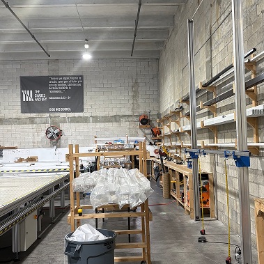 About The Shades Factory: interior of the production workshop featuring a cutting machine and material storage racks used to manufacture custom window coverings.
