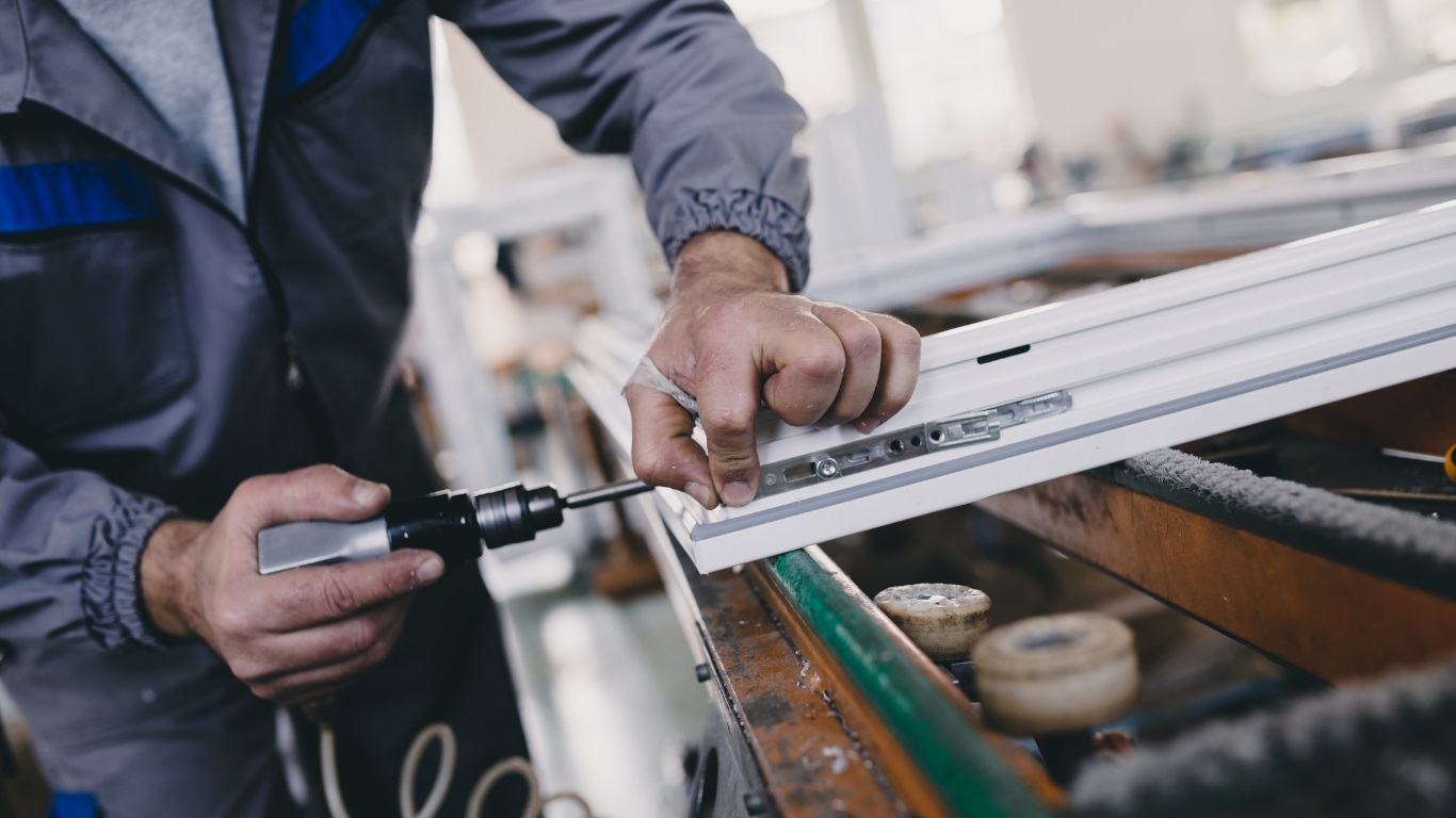 Technician assembling custom blinds and shades in a manufacturing workshop, precisely fastening aluminum components for high-quality custom window treatments.